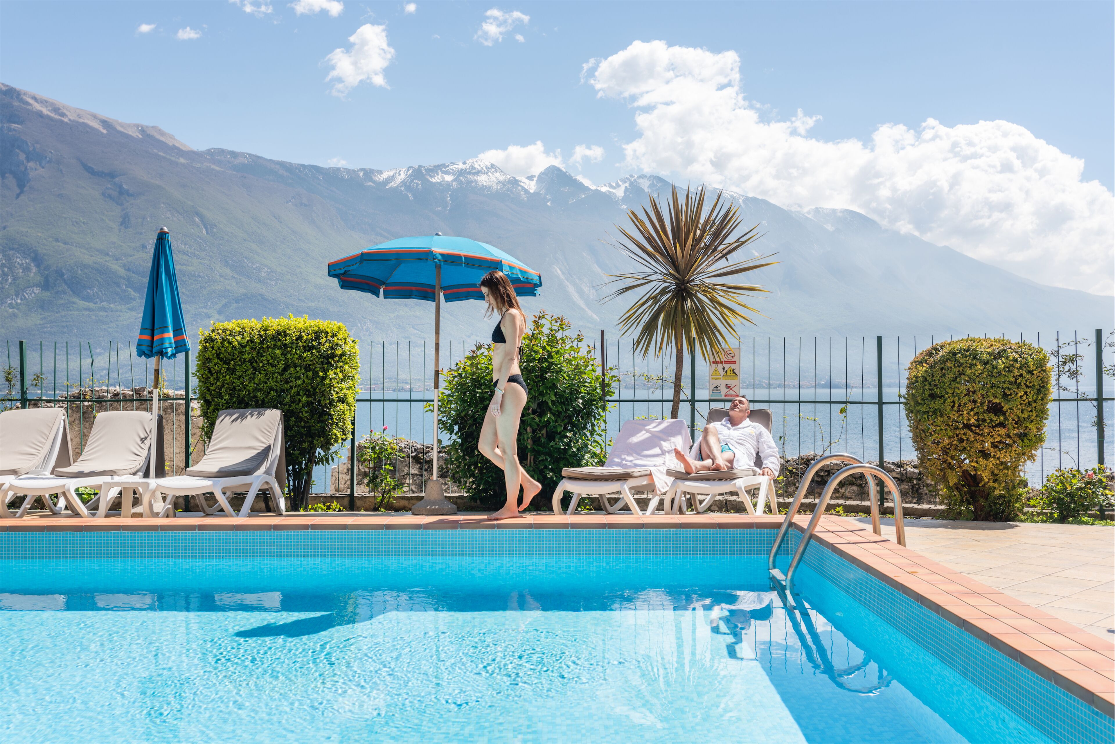 A pool area with lounge chairs, a person walking, and a mountain view in the background.