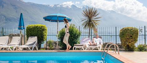 A pool area with lounge chairs, a person walking, and a mountain view in the background.