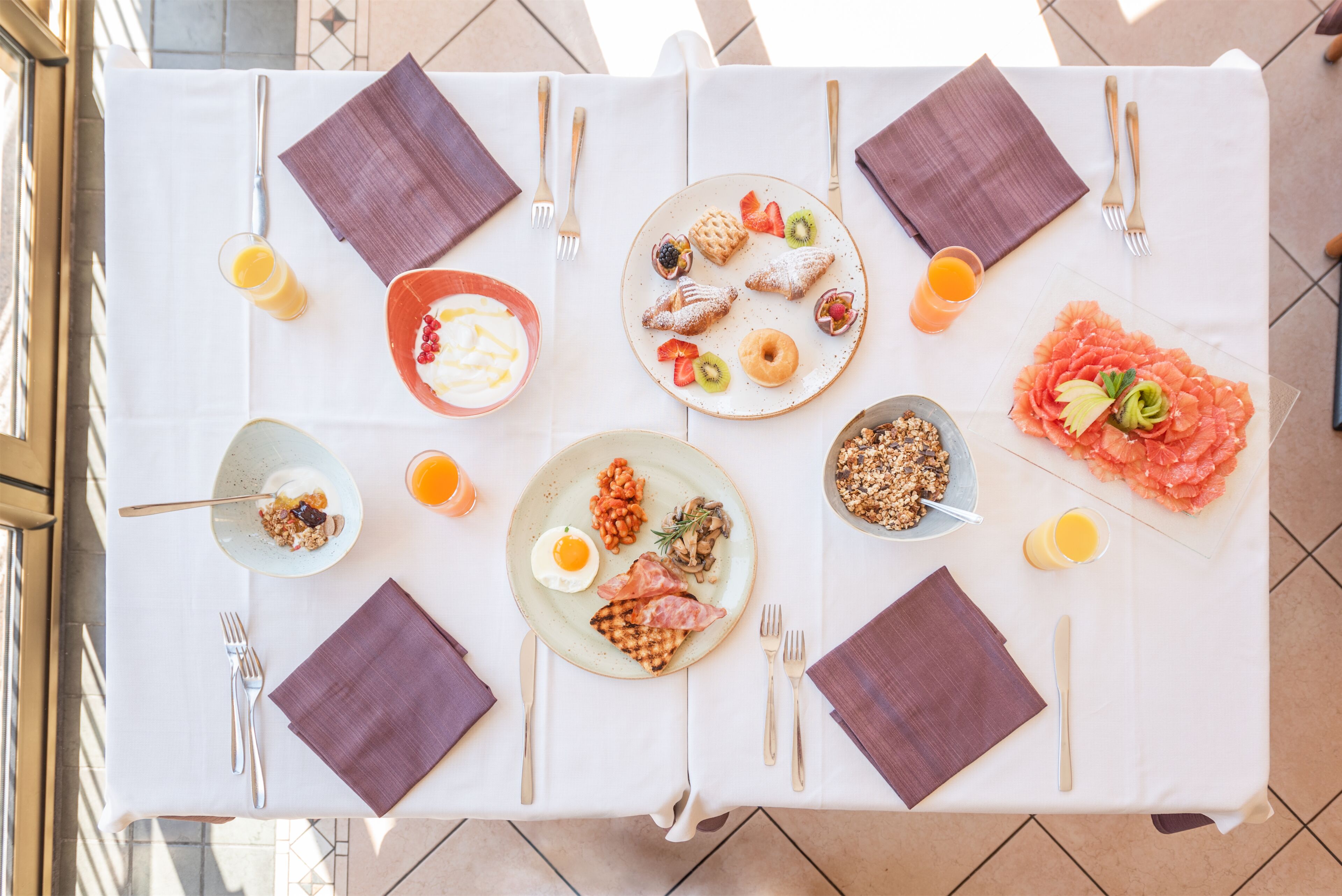 Une table de petit-déjeuner dressée avec des assiettes remplies de nourriture, des couverts et des serviettes.