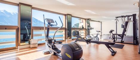 A gym with exercise equipment, large windows, and a view of the sea.