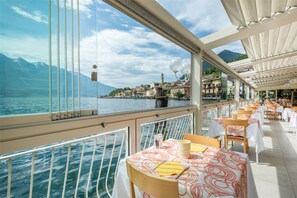 A dining area with tables set for guests, overlooking a body of water and a coastal town. - Hotel le Palme (Limone sul Garda)