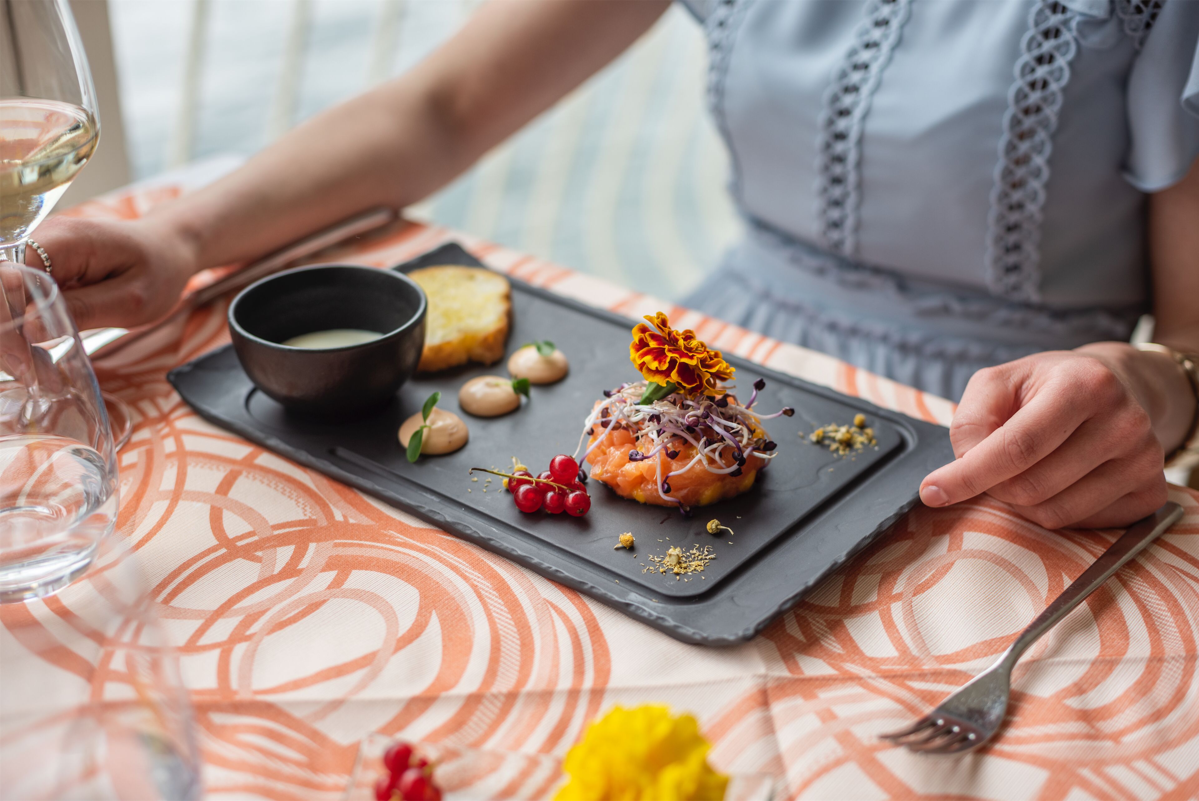 A dining table with a black slate serving tray holding a dessert, a bowl of soup, and some nuts.