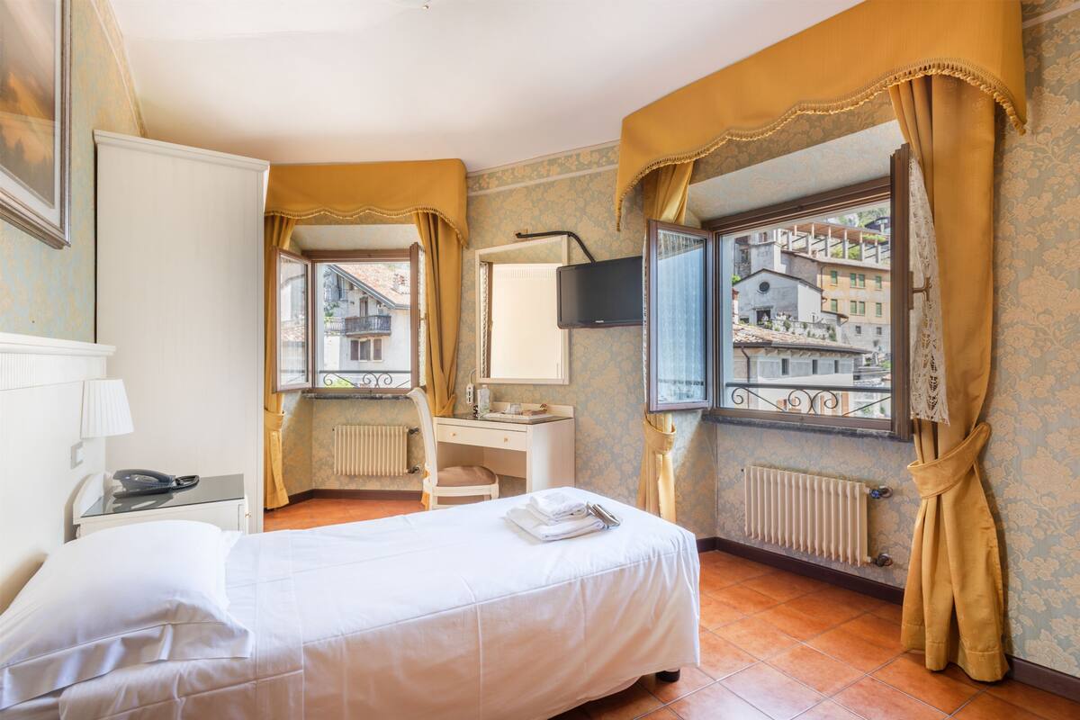 Ein Hotelzimmer mit Bett, Schreibtisch, Stuhl, Fernseher und einem Fenster mit Vorhängen.
