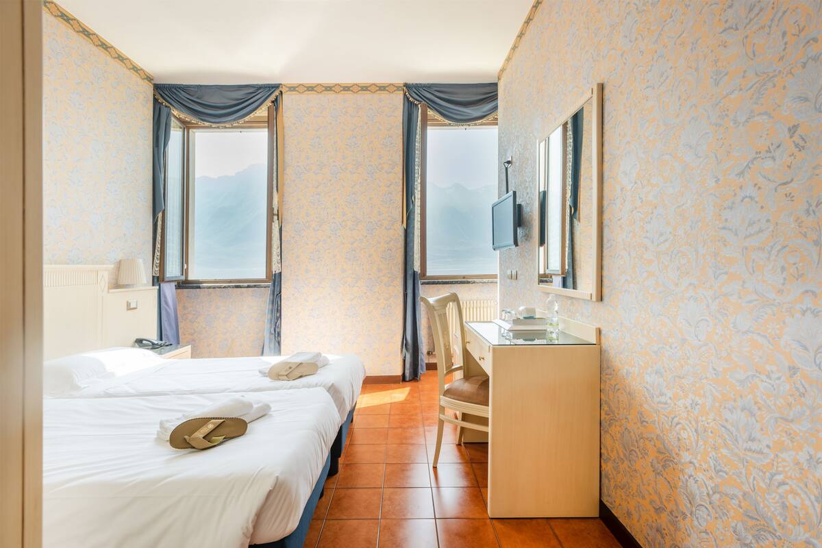 Ein Hotelzimmer mit zwei Betten, einem Schreibtisch, einem Sessel, einem Fernseher und Bergblick durch die Fenster.