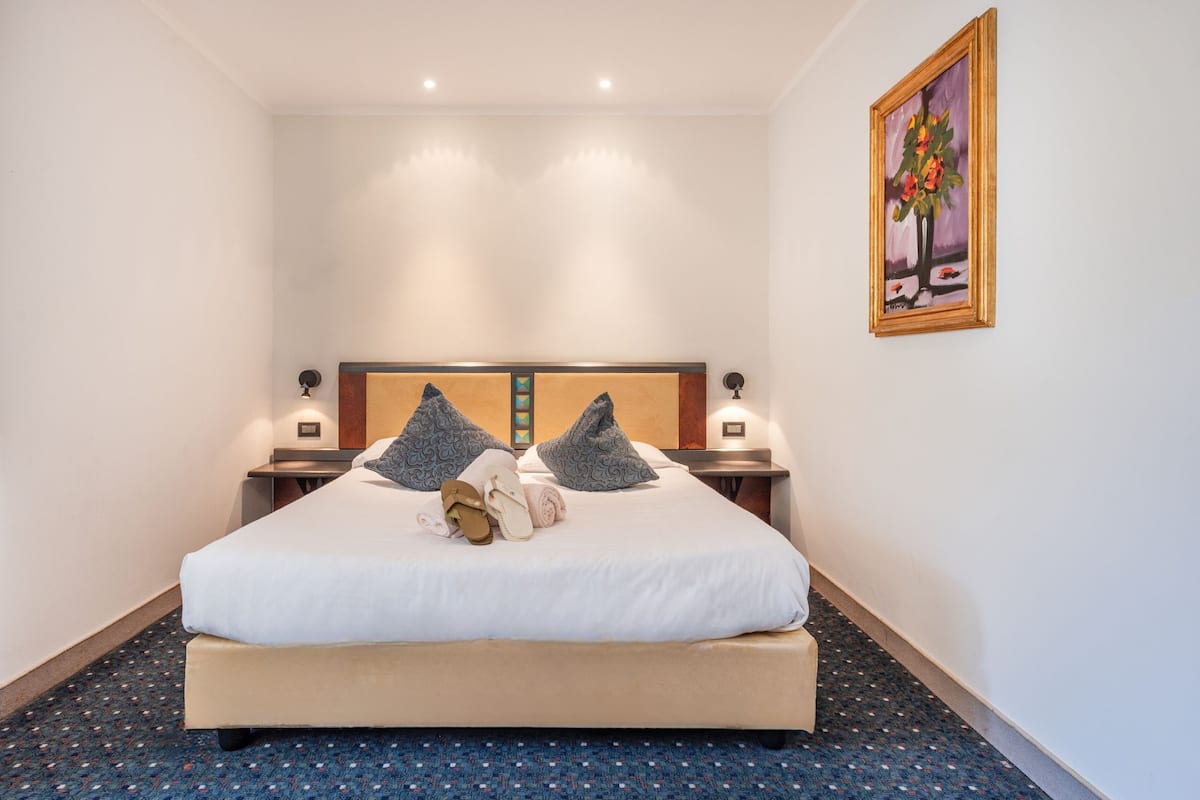 Une chambre d’hôtel avec un grand lit, deux tables de chevet, une tête de lit et un tableau au mur.