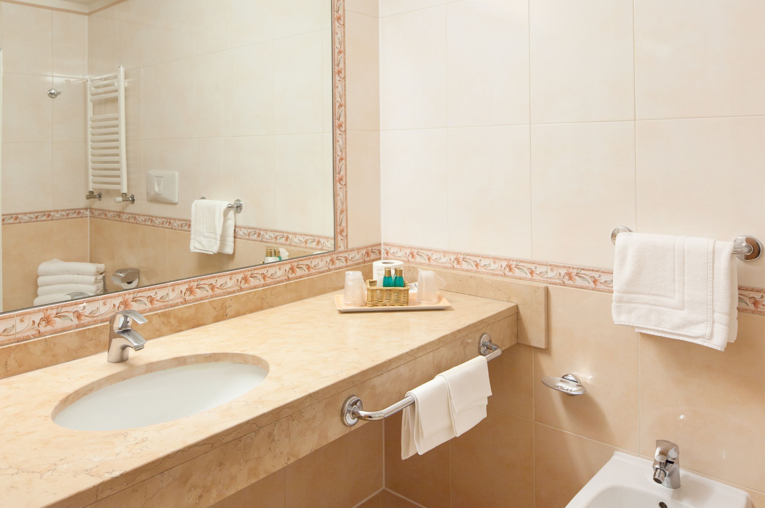 A bathroom with a sink, mirror, towel rack, and a shower area.