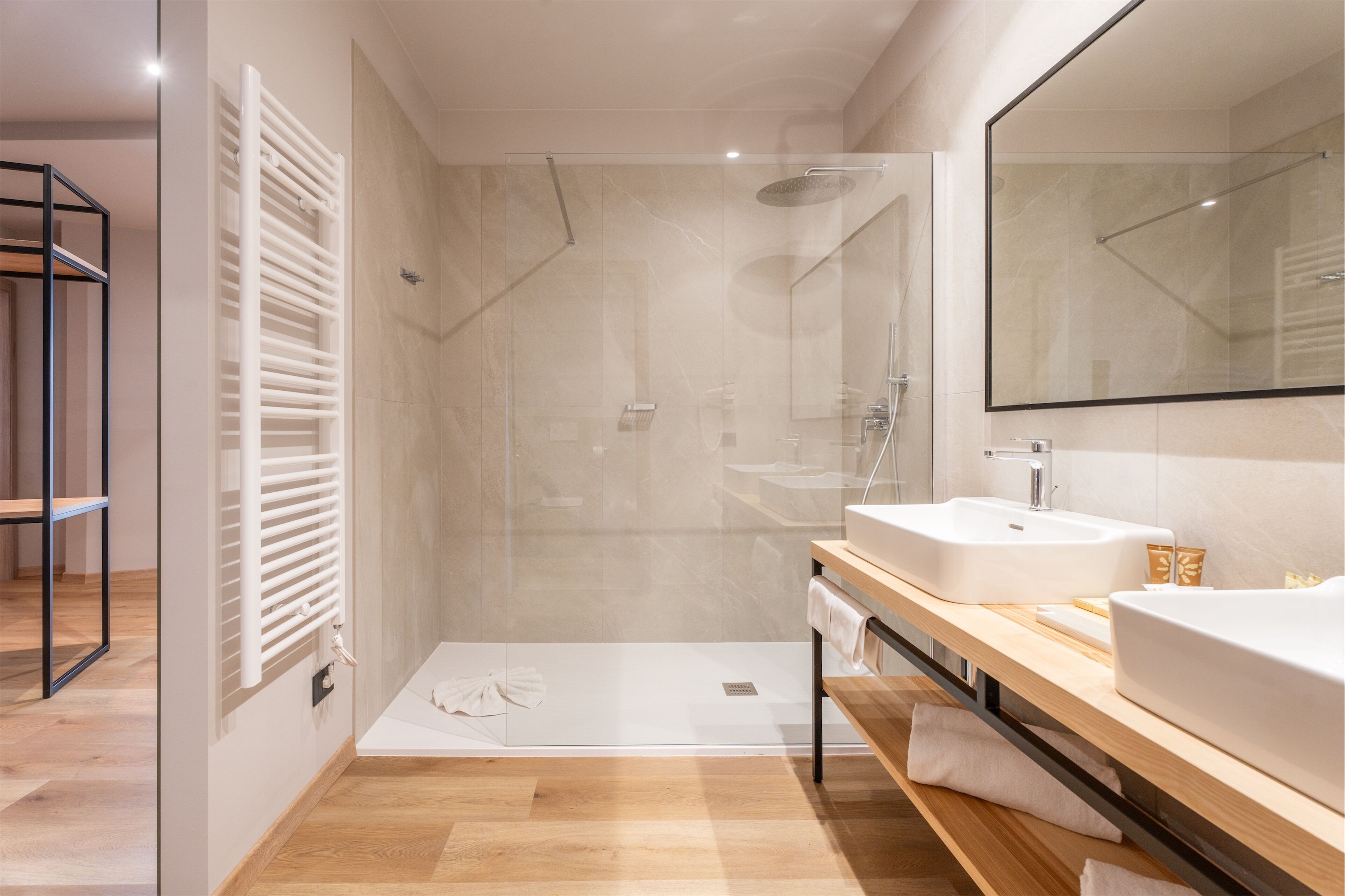 A modern bathroom with a glass-enclosed shower, a large mirror, and a wooden vanity with two sinks.