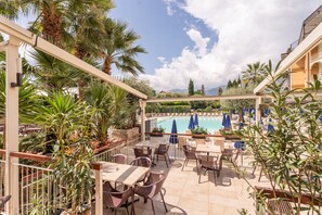 A poolside area with outdoor seating and umbrellas, surrounded by palm trees and plants. - Hotel Majestic Palace (Malcesine)