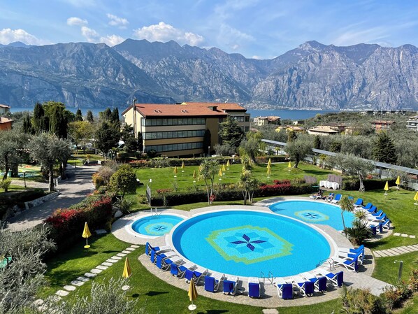 A resort with a large pool area, multiple lounge chairs, and a view of mountains. - Hotel Majestic Palace (Malcesine)