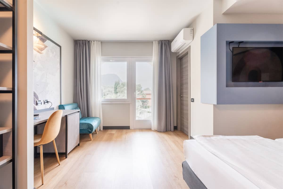 Une chambre d’hôtel moderne équipée d’un lit, d’un bureau avec une chaise, d’un téléviseur fixé au mur et d’une grande fenêtre avec des rideaux.