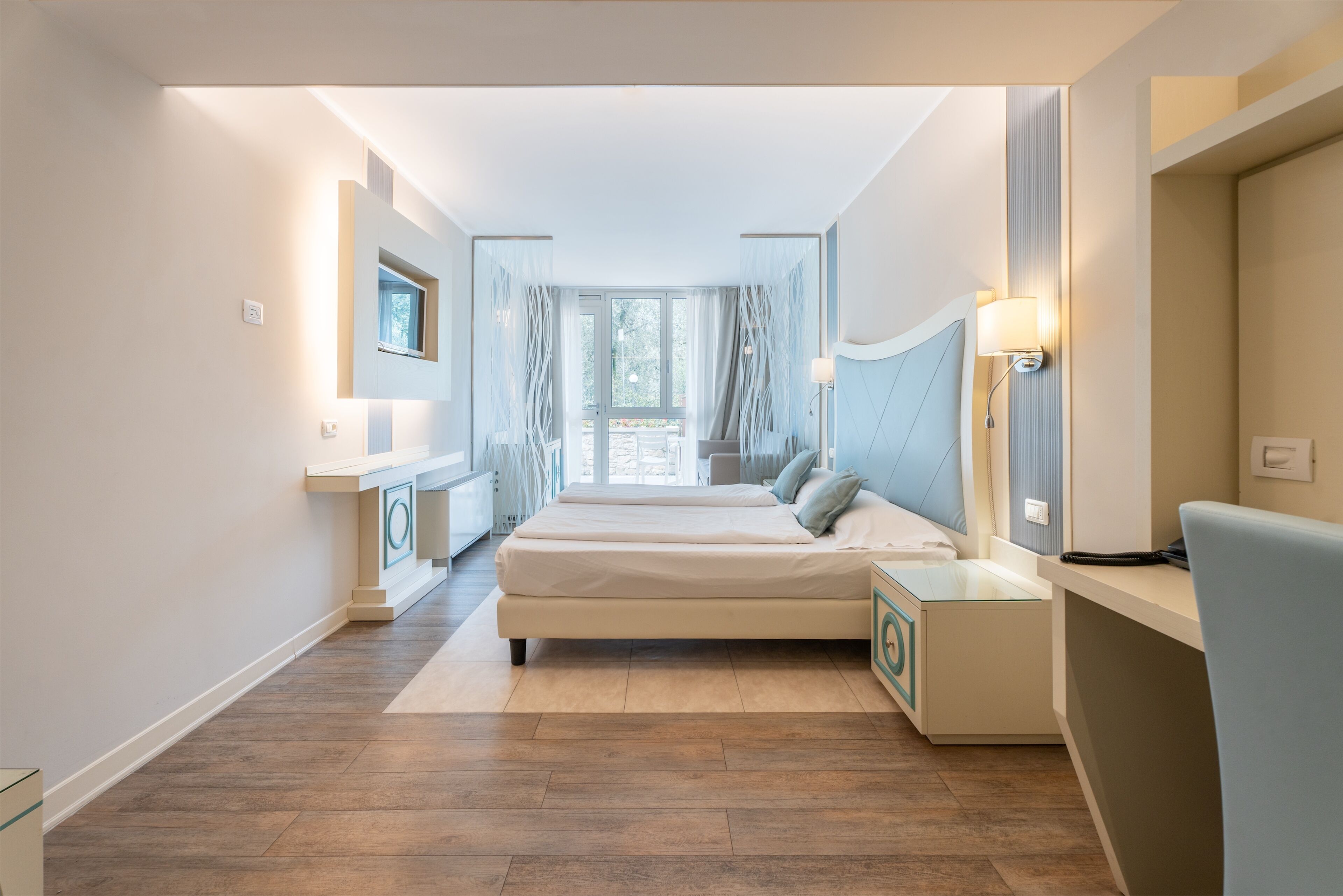 A modern hotel room with a large bed, bedside tables, a desk, and a view of the outdoors.