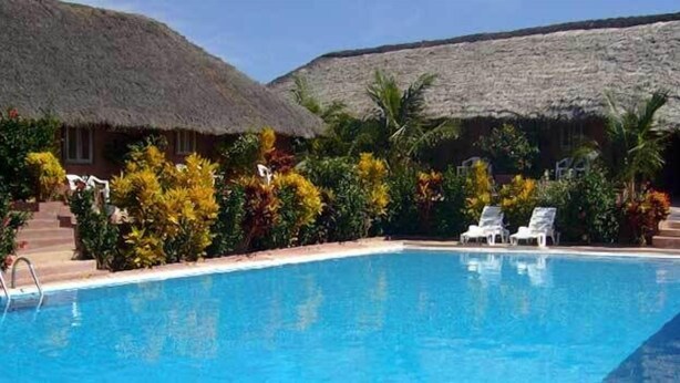 A swimming pool with lounge chairs, surrounded by tropical plants and thatched-roof buildings. - Hotel Maya (Cap Skirring)