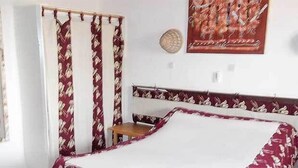 A bedroom with a bed, a mirror, a wardrobe, and a painting on the wall. - Hotel Maya (Cap Skirring)