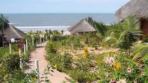 A pathway leading to thatched-roof huts with a beach view. - Hotel Maya (Cap Skirring)