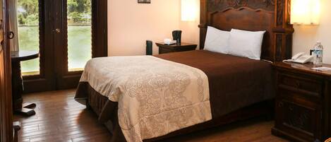 Un dormitorio con una cama grande, cabecera de madera, lámparas de noche, una mesita de noche y vistas a un jardín a través de una puerta.