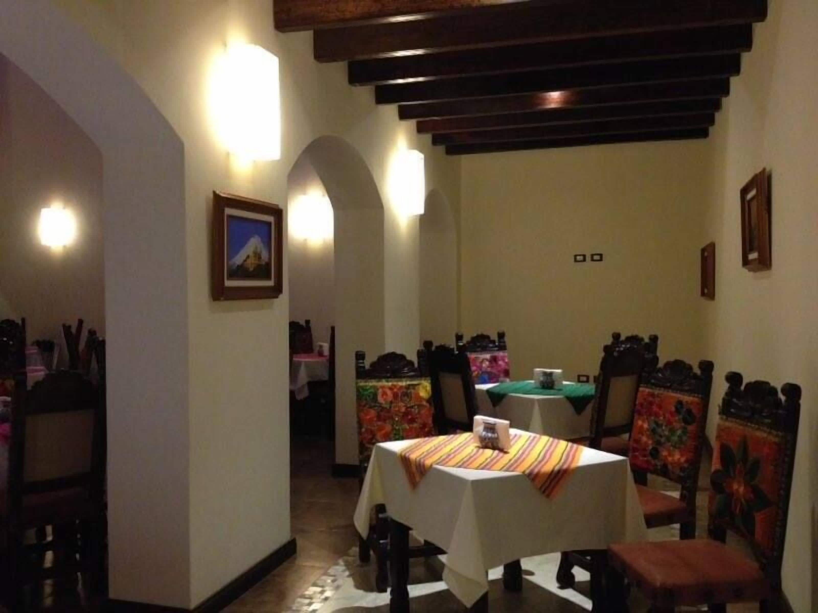 Un comedor con sillas y mesas de madera, un cuadro en la pared y una escalera que sube a otra habitación.