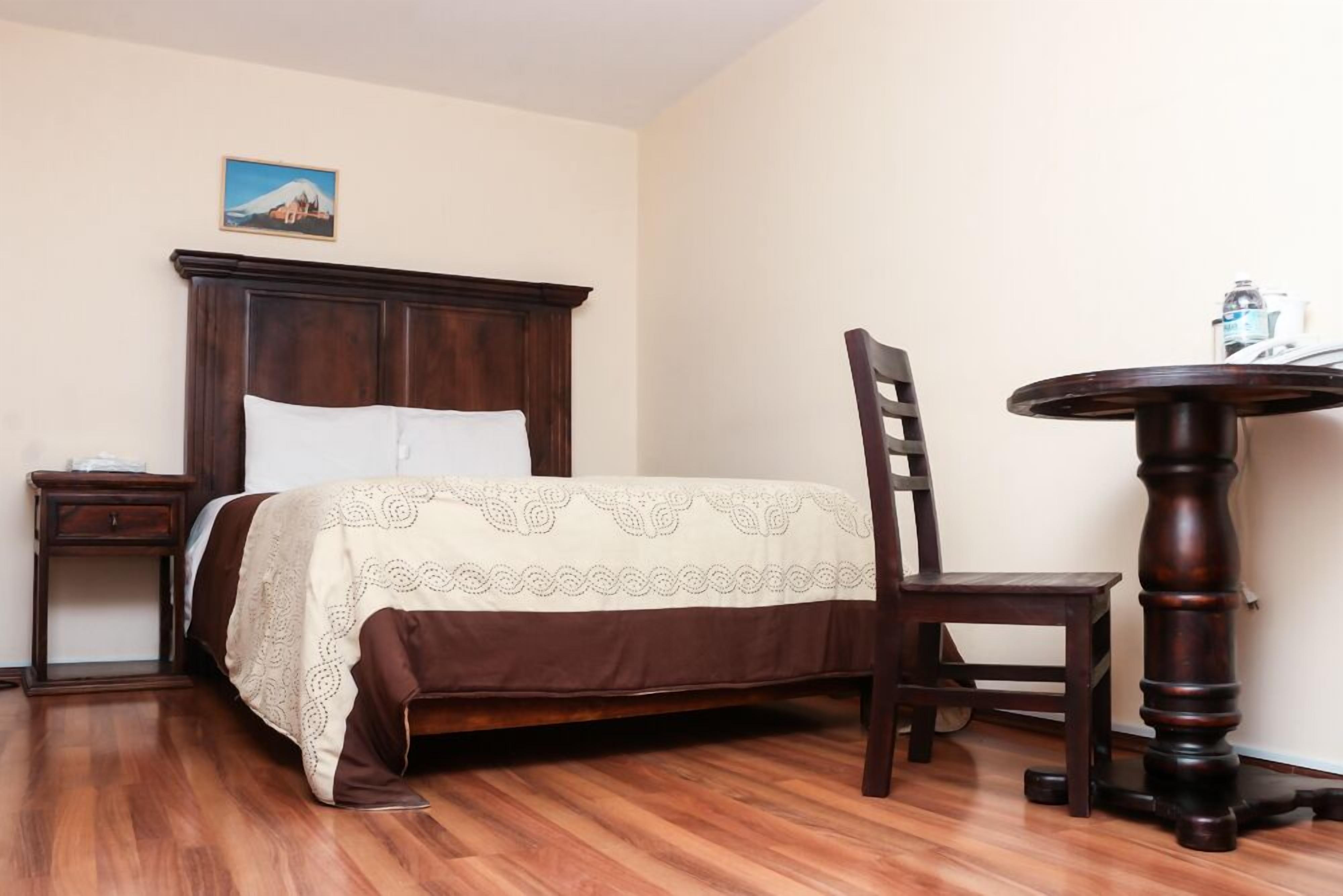 Un dormitorio con una cama de madera, una mesita de noche, una silla y una mesa redonda.