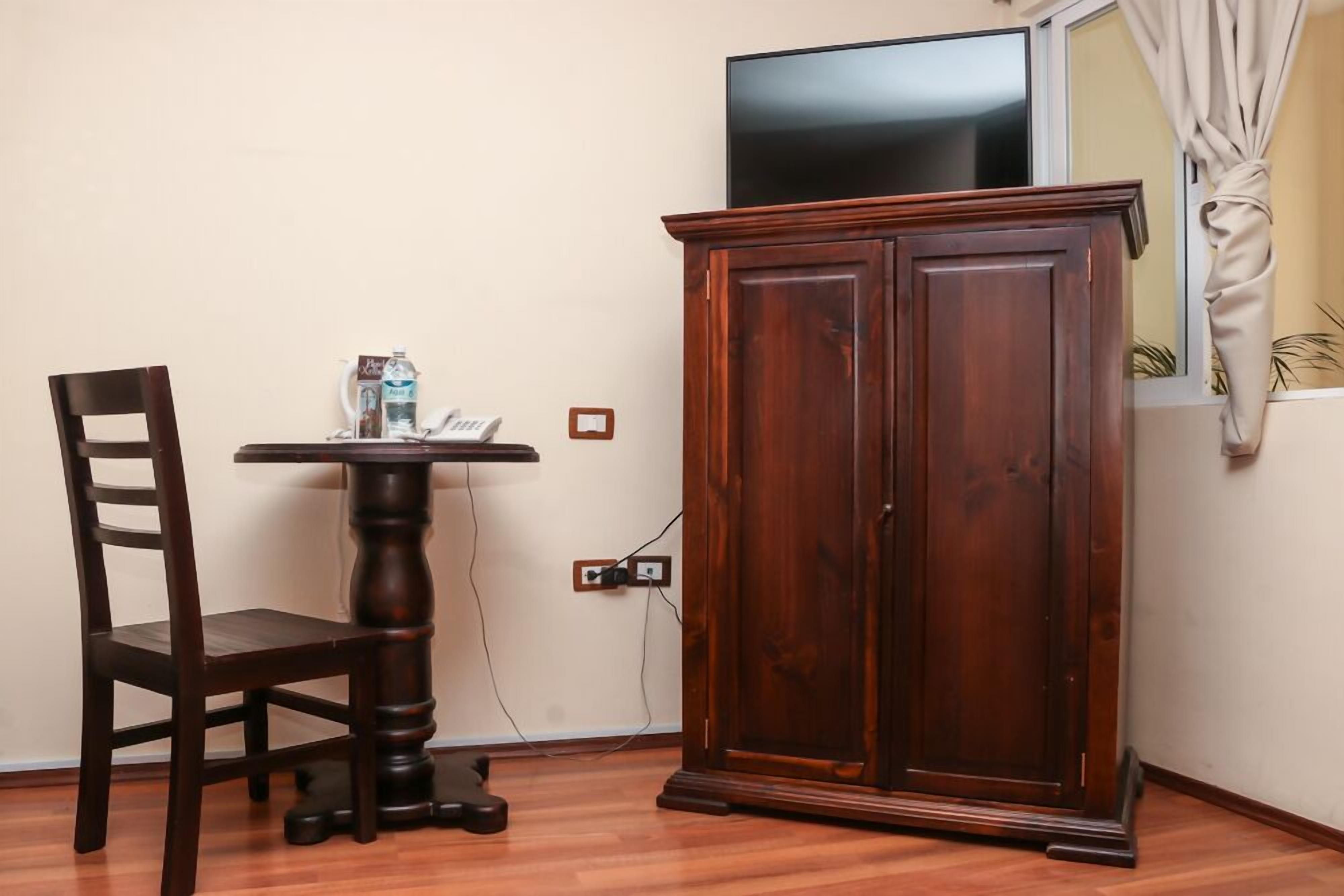 A room with a wooden cabinet, a table with a chair, and a television on the wall.