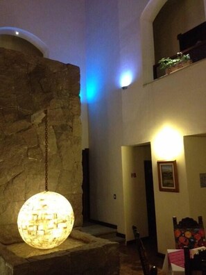 A lobby with a stone wall, a hanging spherical light fixture, and a staircase leading to an upper level. - Hotel Xelhua (San Pedro Cholula)