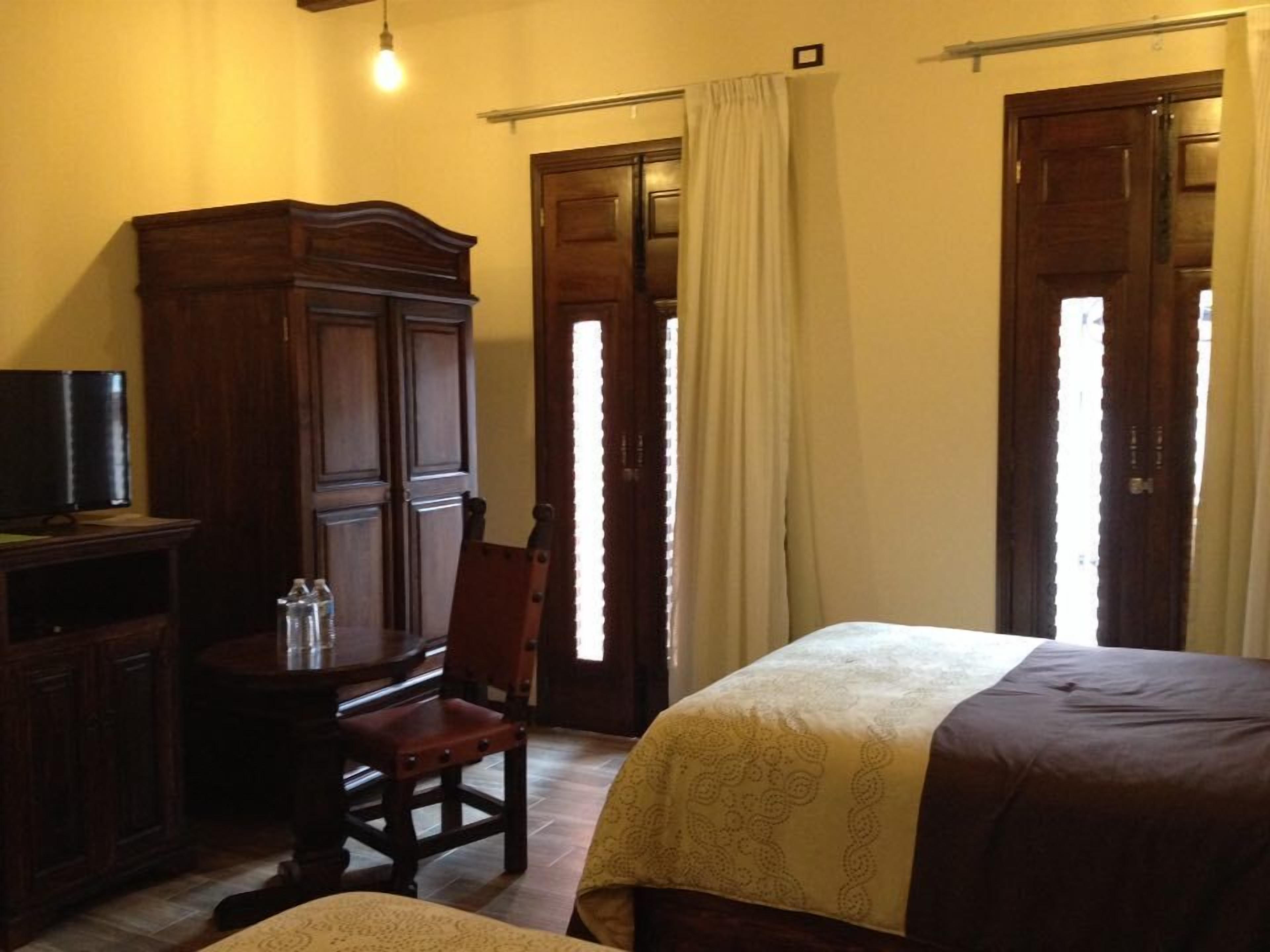 A hotel room with a bed, a wooden wardrobe, a desk with a chair, and a television.