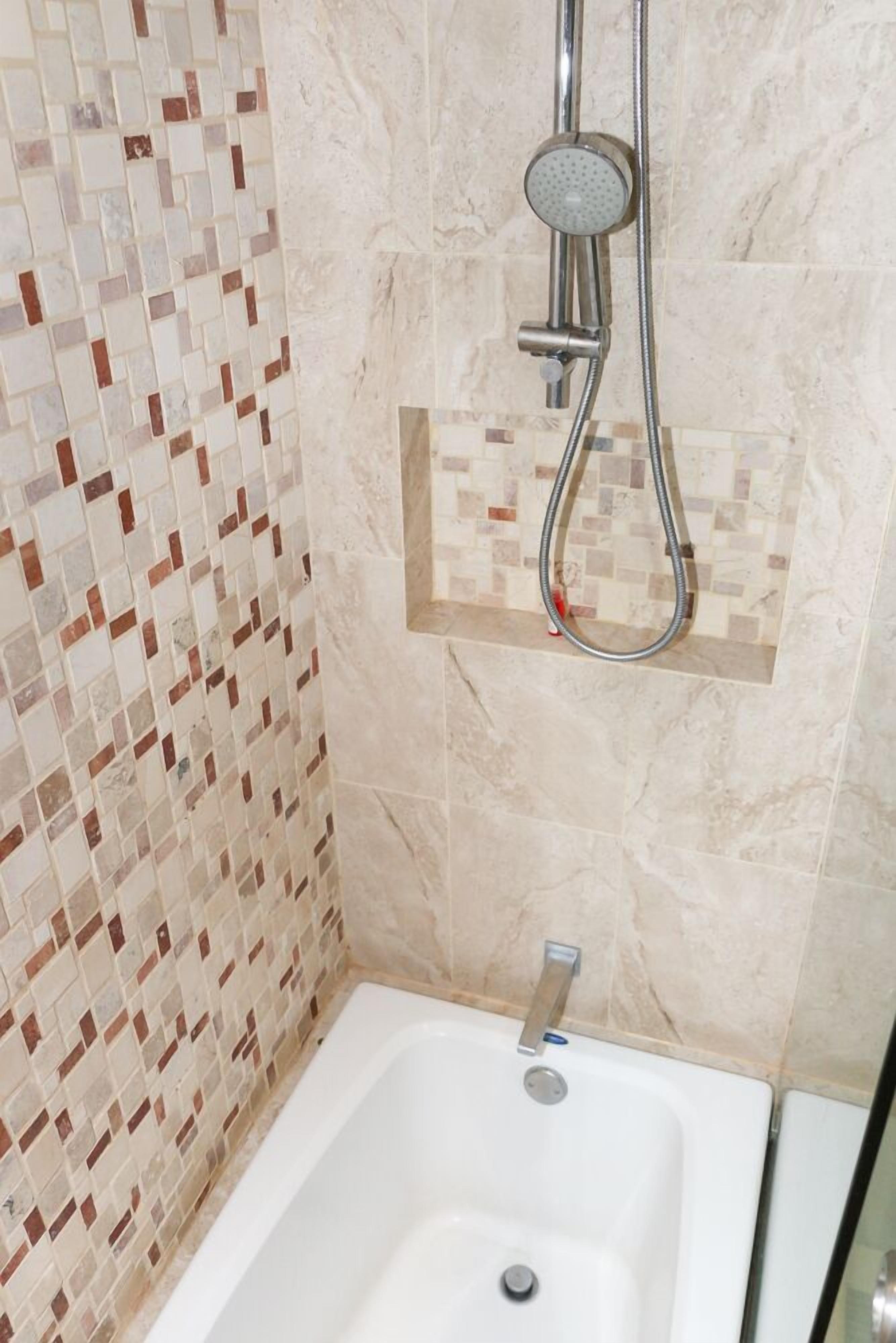A bathroom with a mosaic tile wall, a showerhead, and a bathtub.