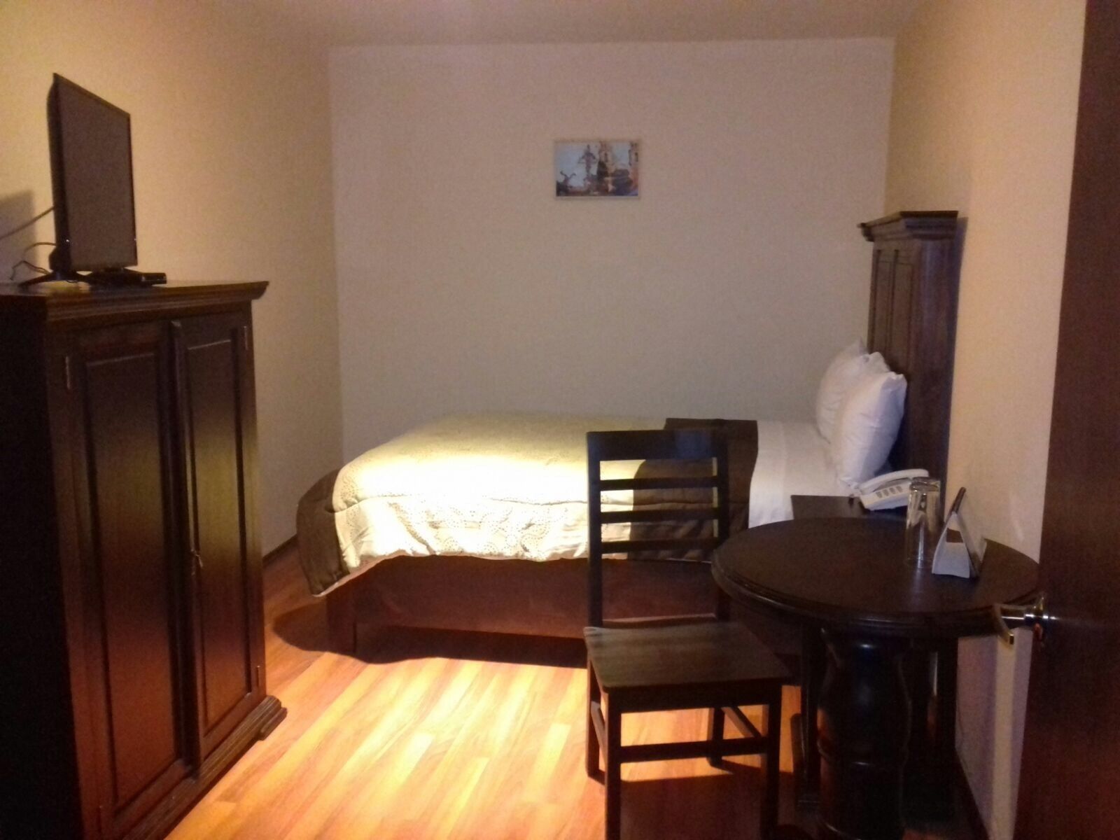 Een kleine, zwak verlichte kamer met een bed, een stoel, een tafeltje en een kast.