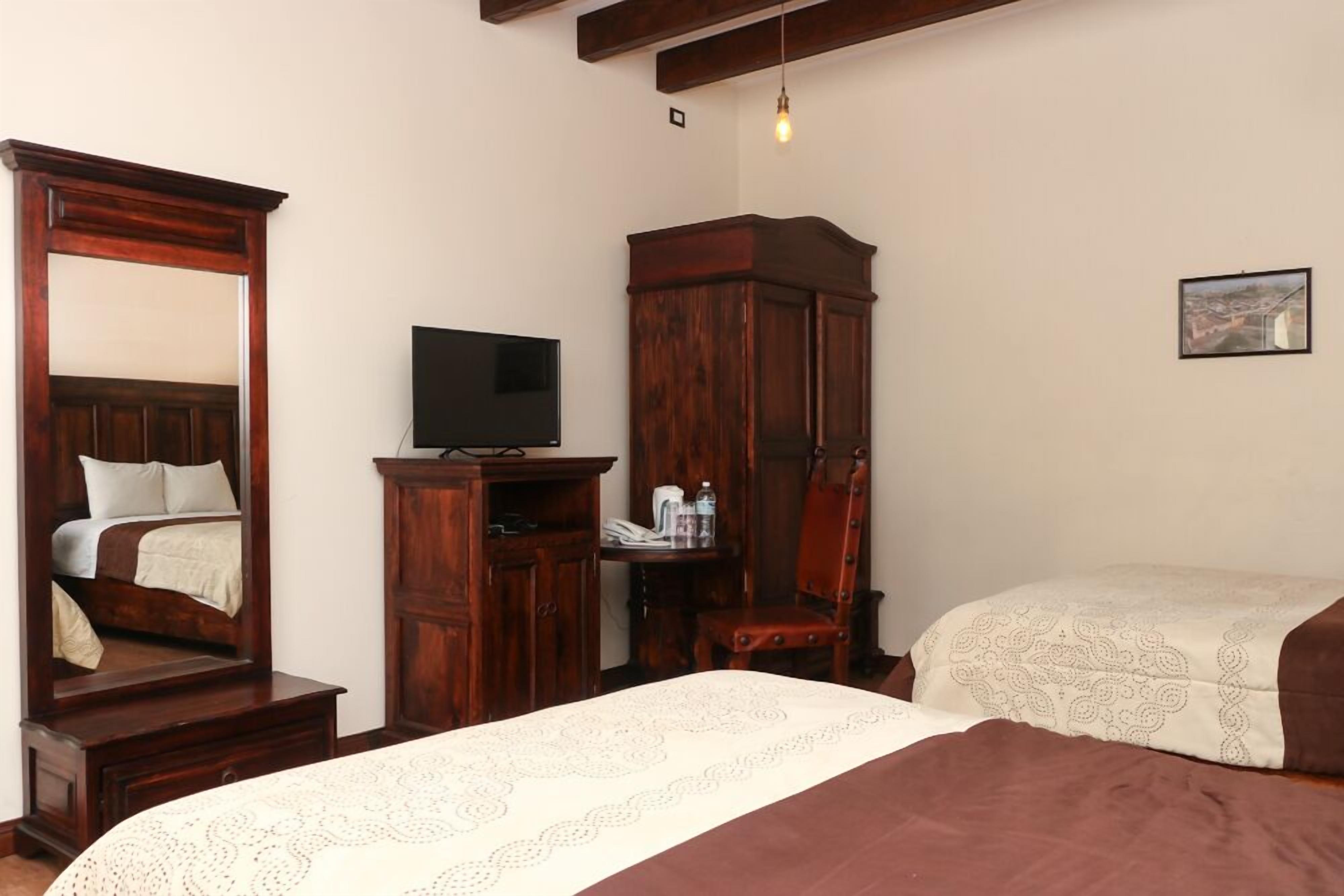 A bedroom with a large mirror, wooden wardrobe, a television, and a bed with patterned bedding.