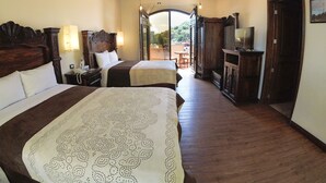 A hotel room with two beds, wooden headboards, a television, and a balcony with a table and chairs. - Hotel Xelhua (San Pedro Cholula)