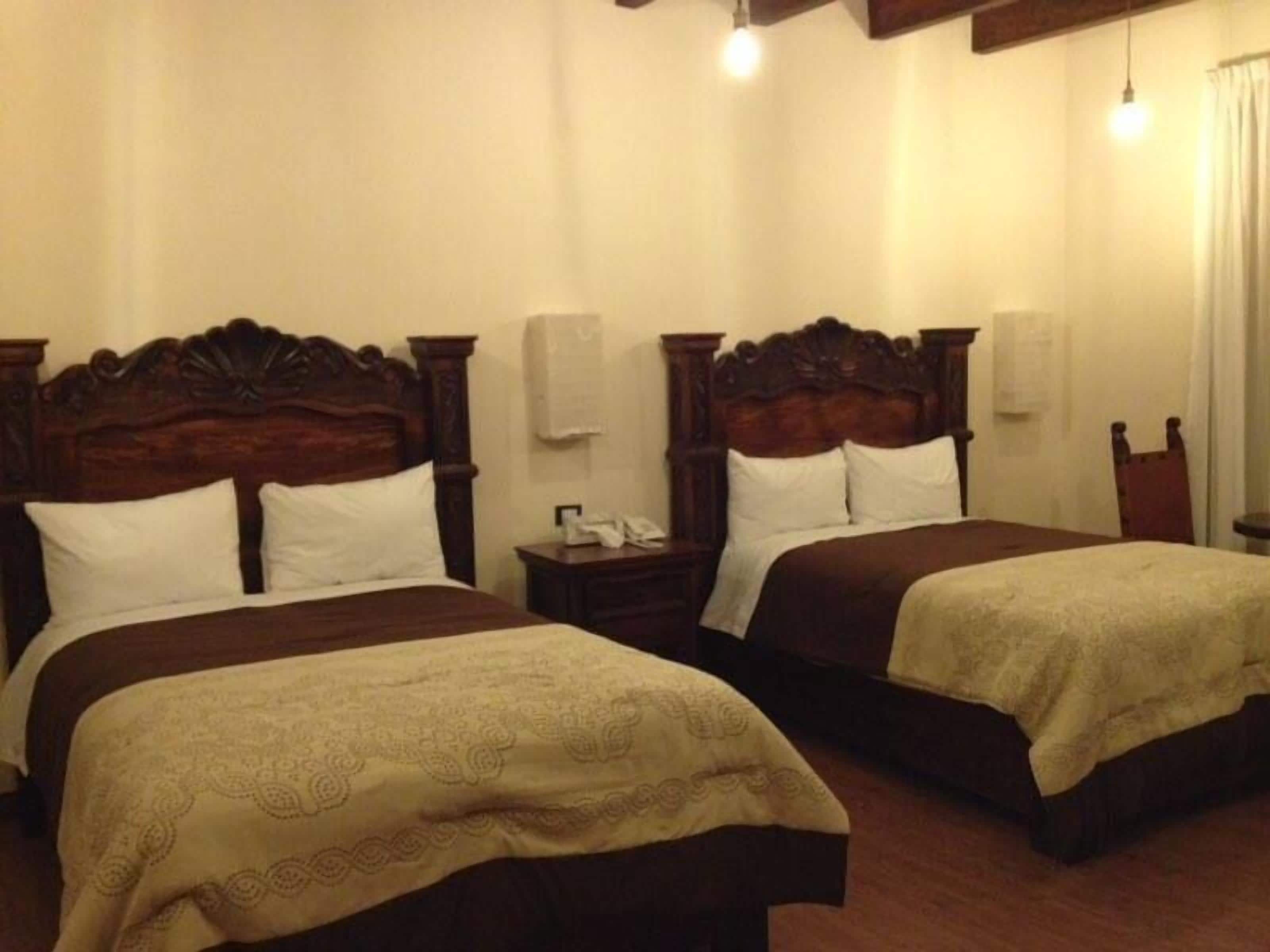 A hotel room with two beds, wooden headboards, and bedside tables with lamps.