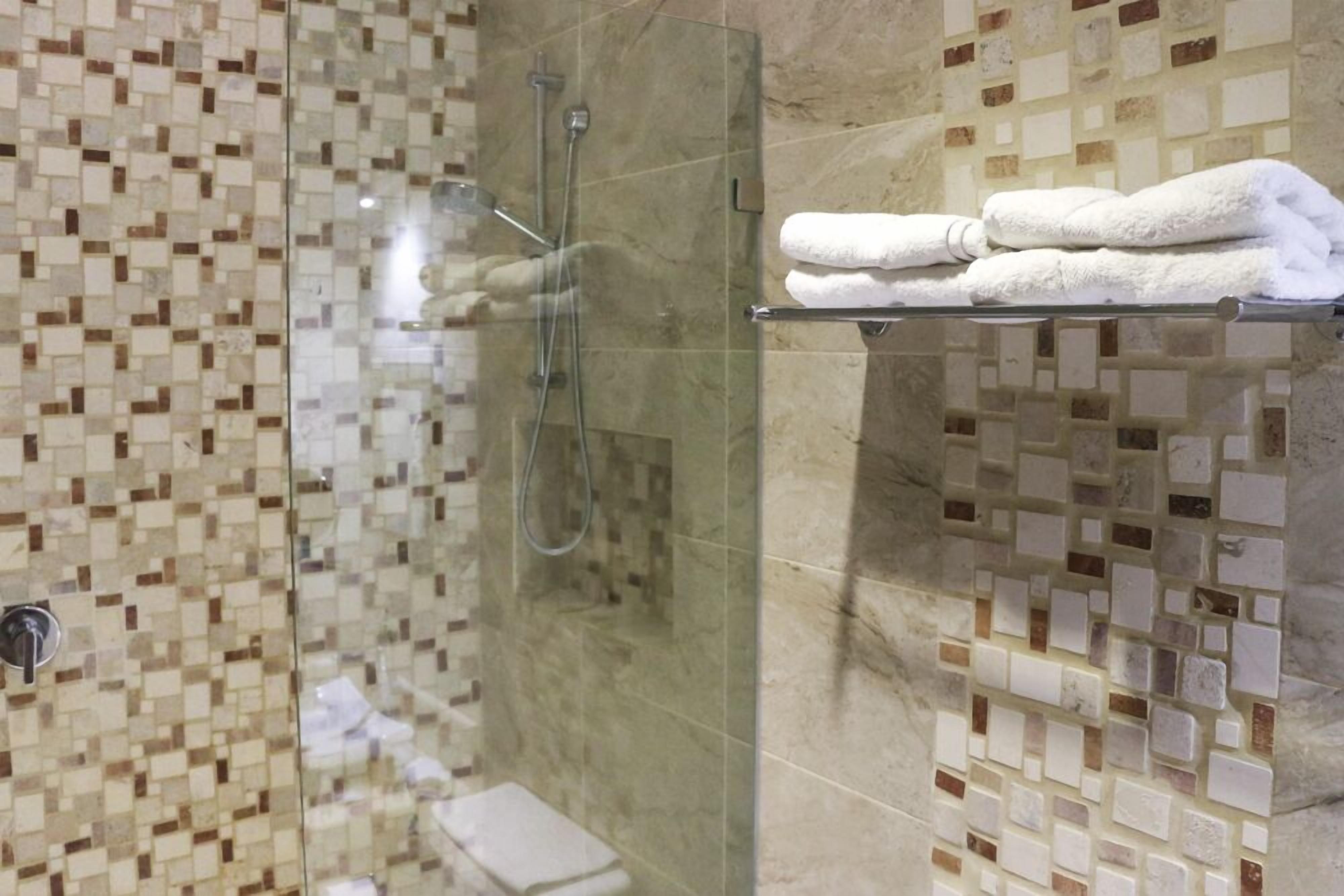Una cabina doccia in vetro con parete rivestita in mosaico, uno scaffale in vetro con asciugamani piegati e un water a vista.