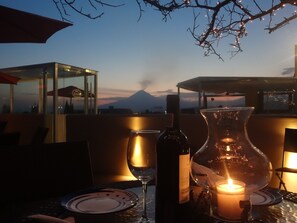 A table with a candle, a wine bottle, and a glass. In the background, there is a mountain and a clear sky. - Hotel Xelhua (San Pedro Cholula)