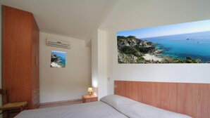 A bedroom with a bed, a nightstand with a lamp, a wooden wardrobe, and a wall-mounted air conditioner. - Hotel Residence Rosy (Ricadi)