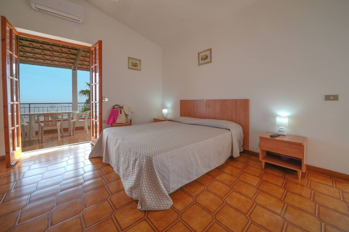 Ein Schlafzimmer mit Bett, Nachttisch und Blick ins Freie.