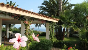 A covered outdoor area with a tiled roof, lush greenery, and a view of the ocean. - Hotel Residence Rosy (Ricadi)