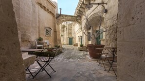 A narrow cobblestone street with stone buildings, a green door, and outdoor seating with tables and chairs. - Casa Diva (Matera)