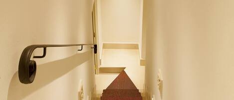 A staircase with a red carpet leading to a landing with a white wall and a stone ceiling.