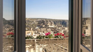 Un balcón con barandillas de metal ornamentadas y vistas a un pueblo histórico con edificios y colinas rocosas al fondo.
