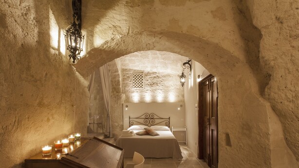 A narrow, arched hallway leading to a bedroom with a bed, a wooden chest, and candles. - Casa Diva (Matera)