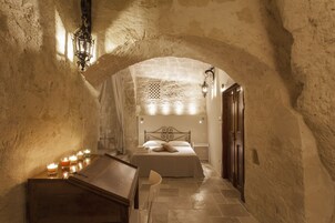 Un estrecho pasillo abovedado que conduce a un dormitorio con una cama, un cofre de madera y velas.