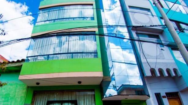 Een meerhoog gebouw met een groene gevel, grote ramen en zichtbare elektriciteitskabels.