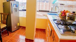 Een kleine keuken met een koelkast, eettafel, stoelen en een raam met uitzicht.