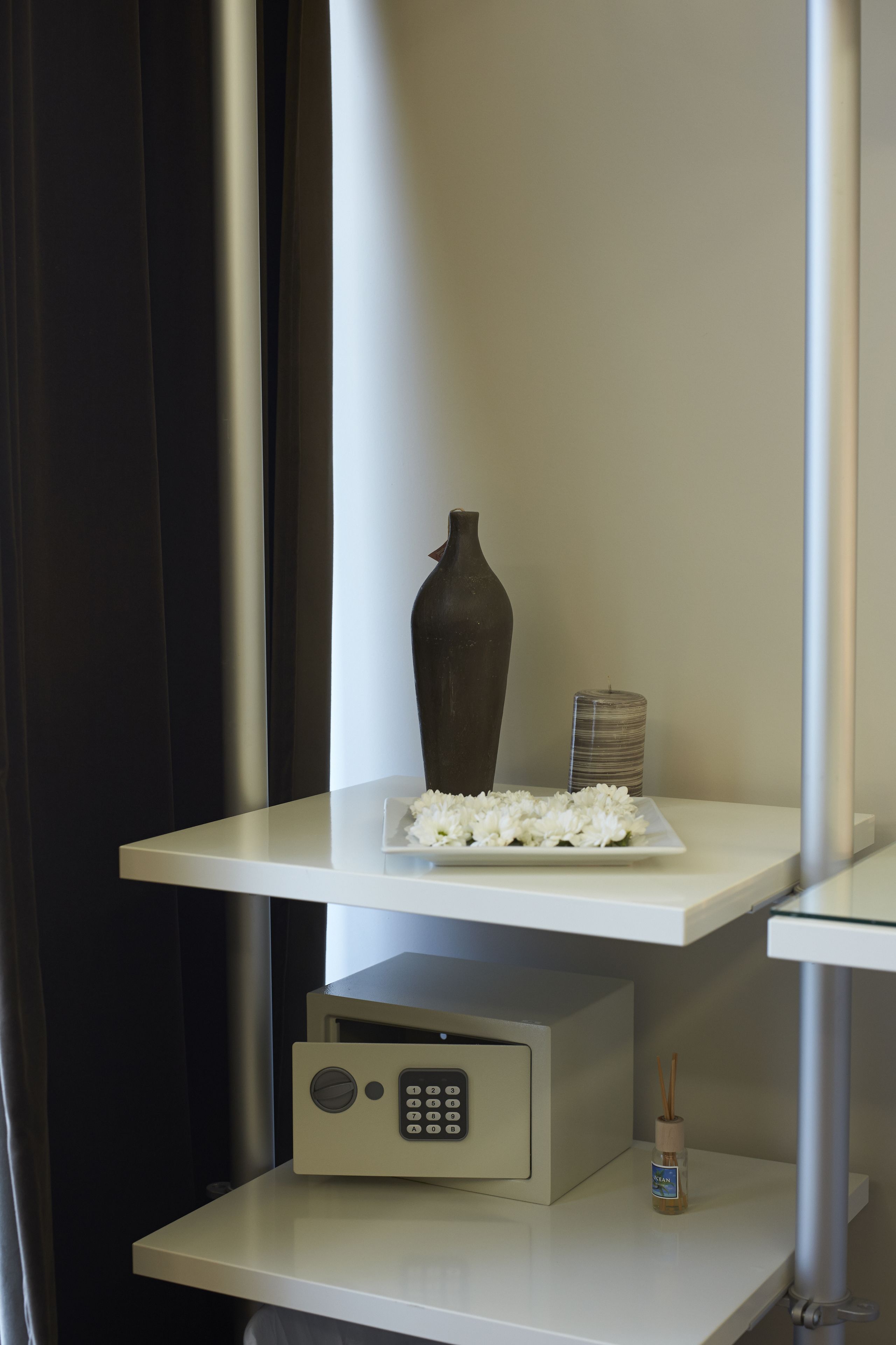 A white shelf with a vase, a candle, and a small dish of white flowers.