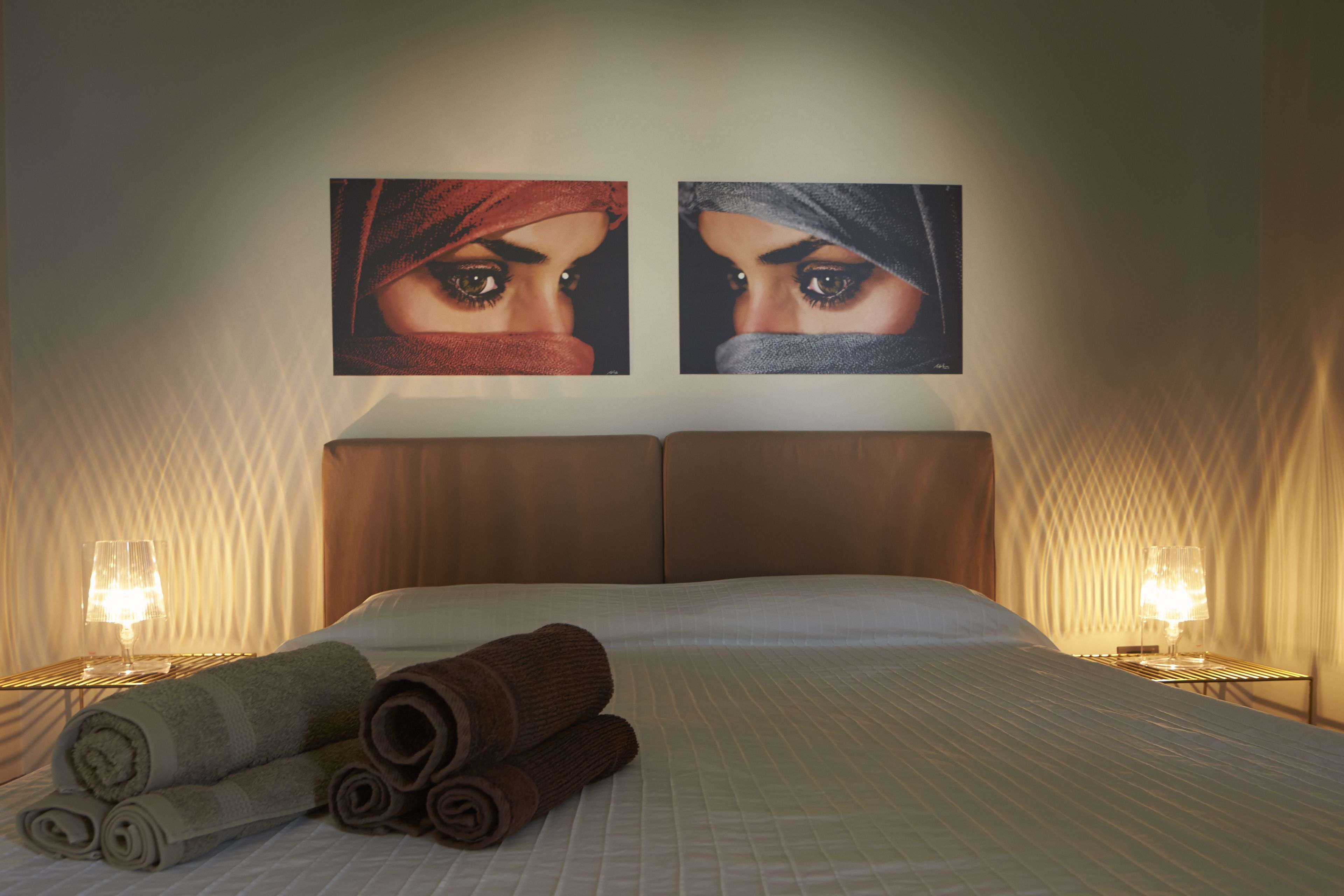 Ein Hotelzimmer mit einem großen Bett, zwei an der Wand befestigten Bildern, einem Nachttisch mit Lampe und zusammengerollten Handtüchern auf dem Bett.