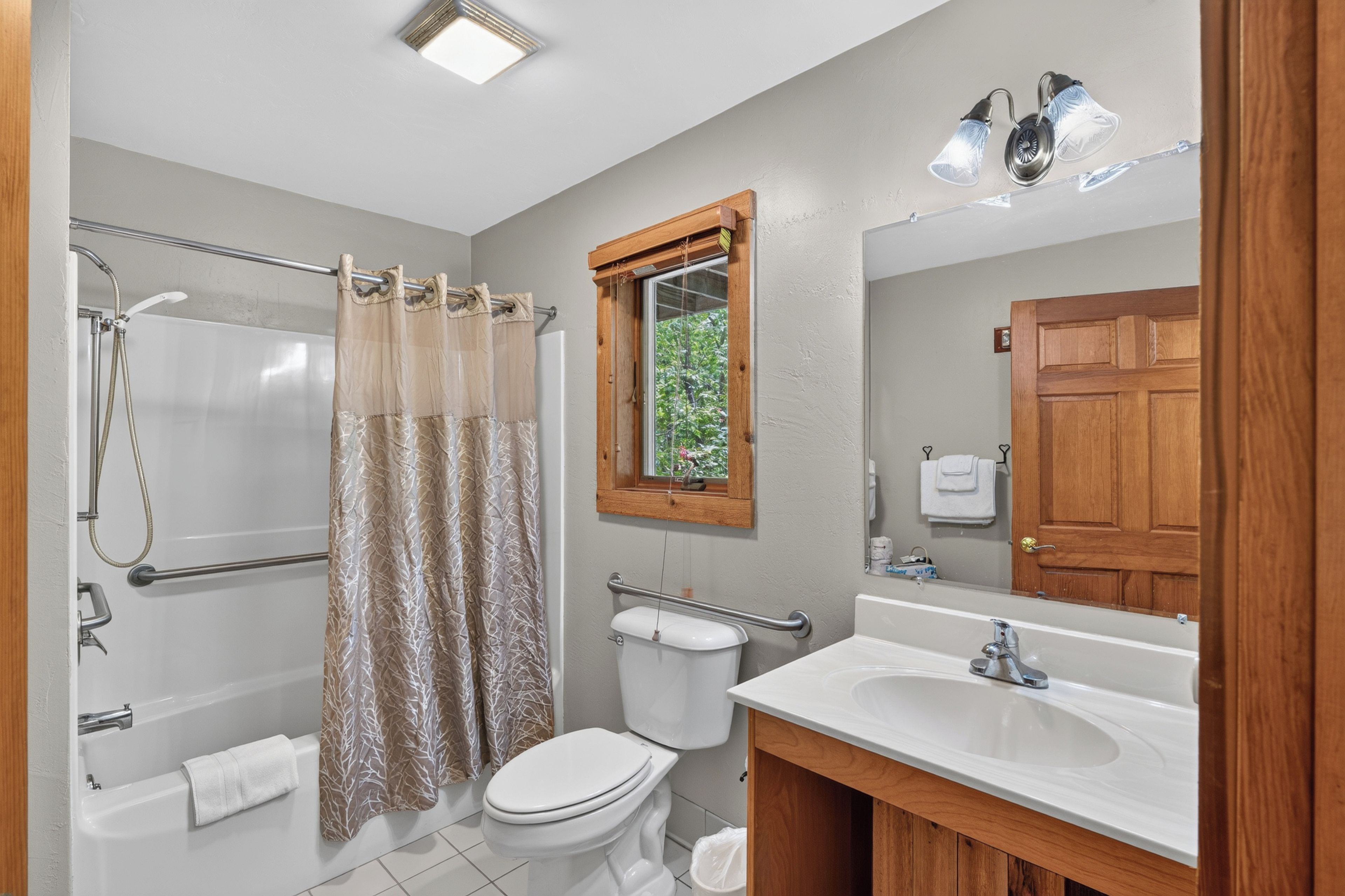 A bathroom with a shower, toilet, sink, and a window with a view of greenery.