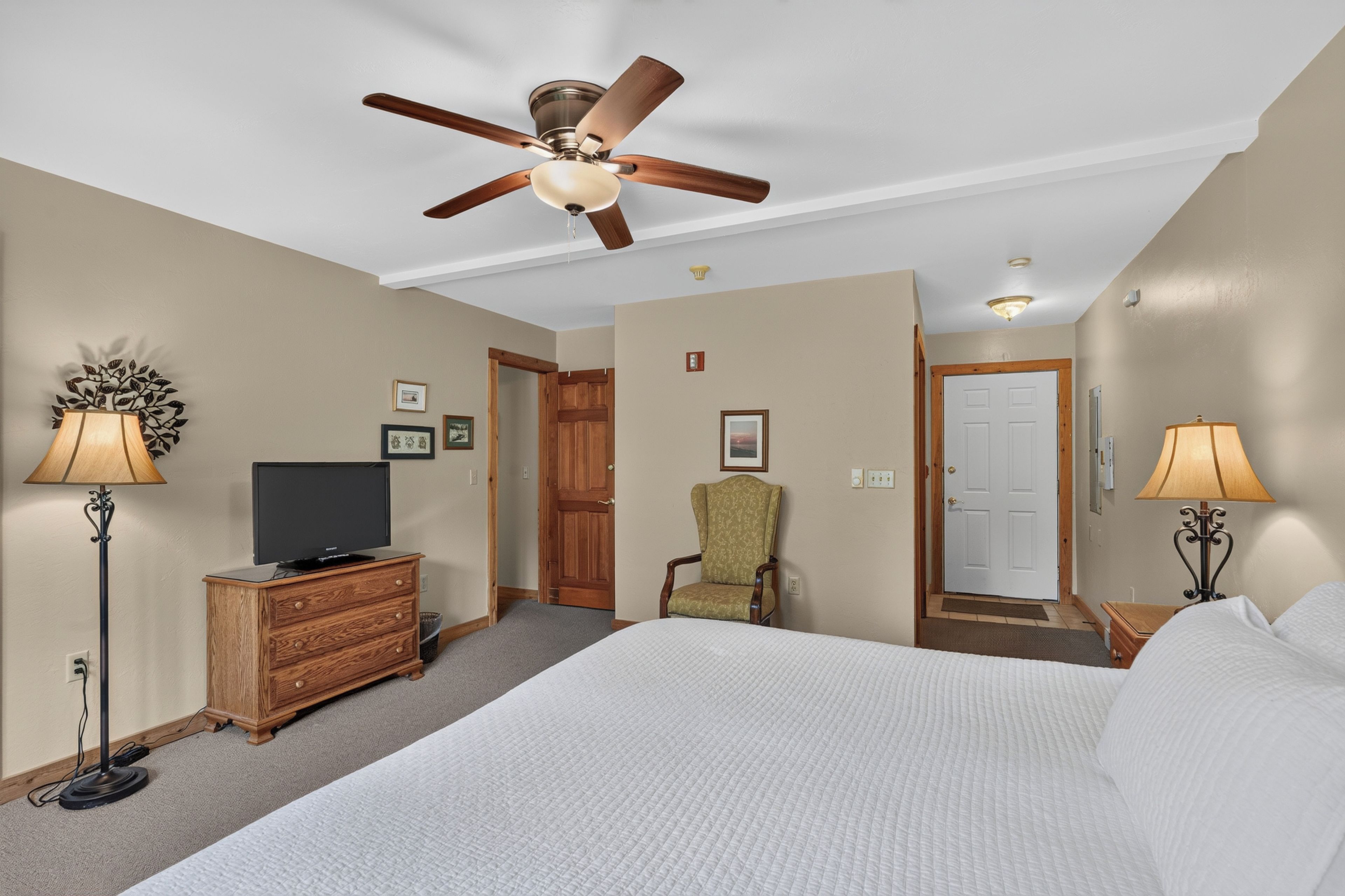 Une chambre d’hôtel équipée d’un lit, d’une télévision, d’une chaise, d’un bureau, d’un ventilateur de plafond et d’une porte.