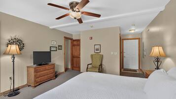 Une chambre d’hôtel équipée d’un lit, d’une télévision, d’une chaise, d’un bureau, d’un ventilateur de plafond et d’une porte.
