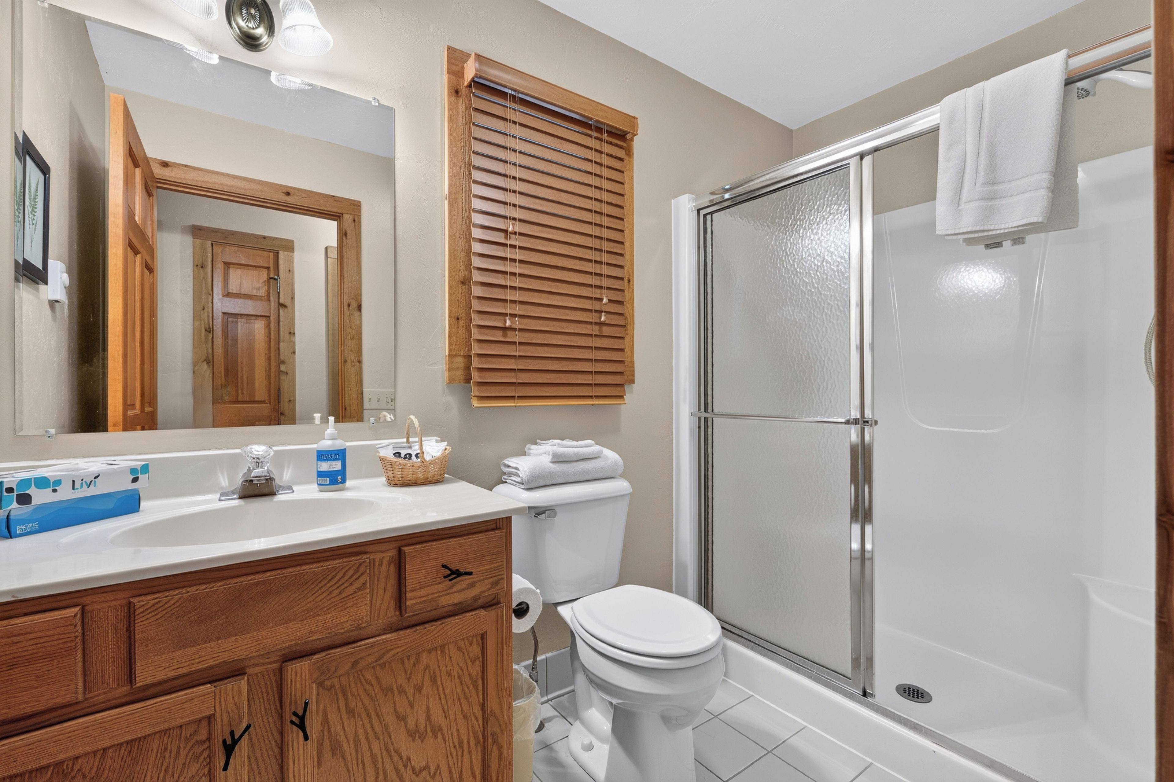 A bathroom with a shower, toilet, sink, and wooden cabinets.