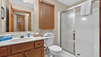 A bathroom with a shower, toilet, sink, and wooden cabinets.