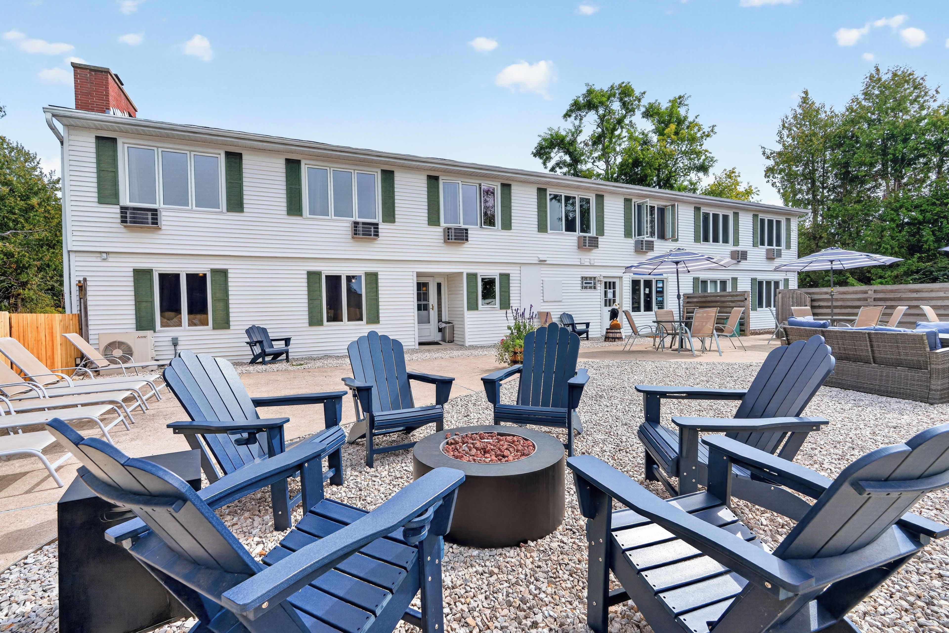 A two-story building with a patio area featuring Adirondack chairs and a fire pit.