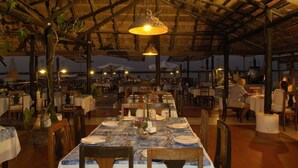 Un restaurante con techo de paja, mesas y sillas de madera dispuestas para comer.